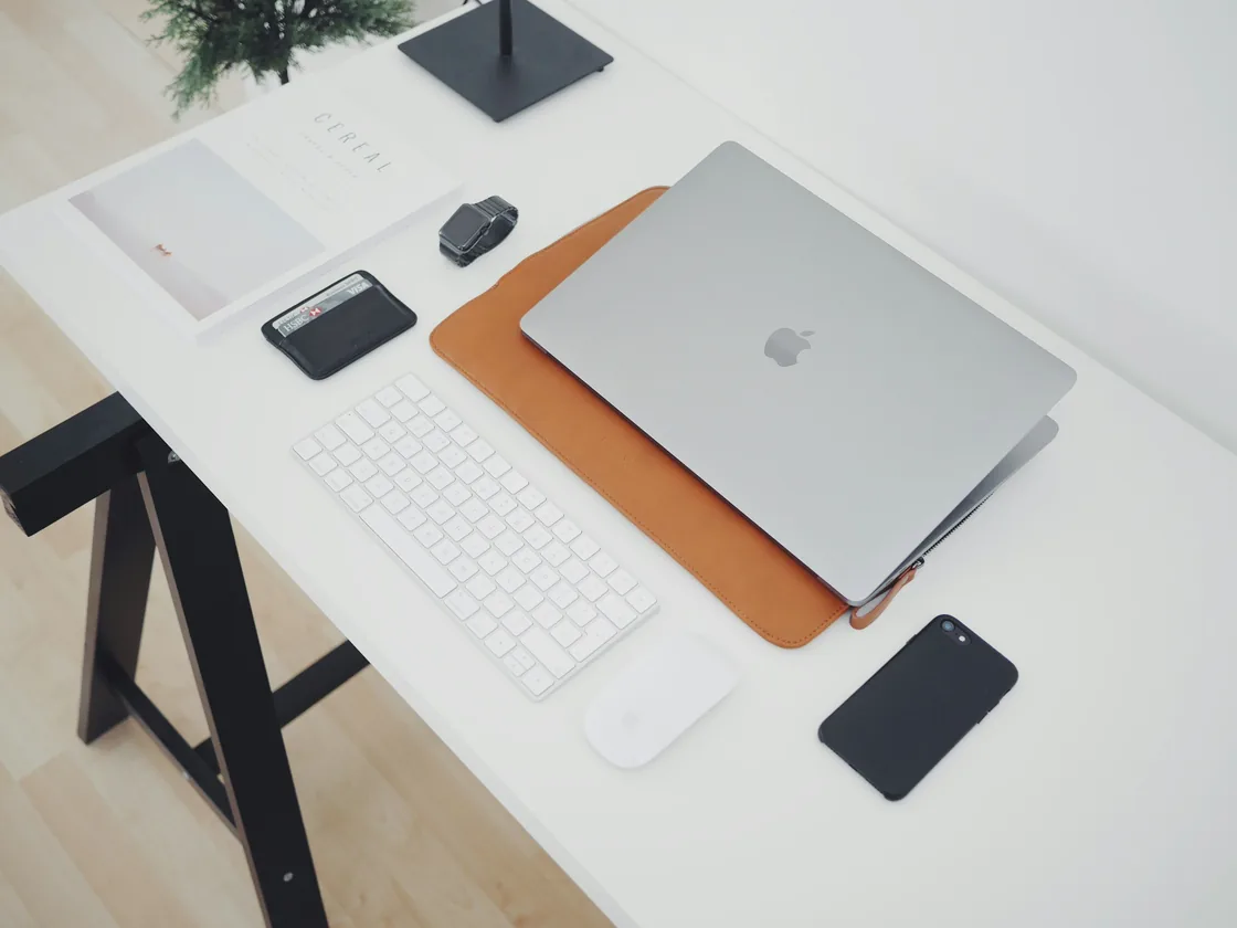 A tidy white desk from above with a laptop, keyboard and phone