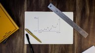 A hand-drawn line graph on paper next to a ruler and two pens