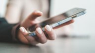 A hand holding a smartphone against a soft, bright background