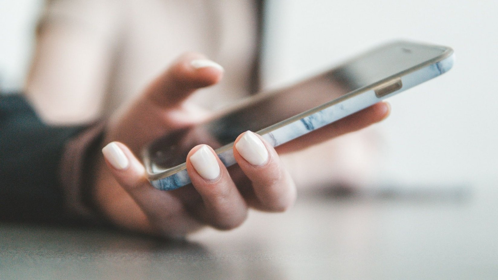 A hand holding a smartphone against a soft, bright background